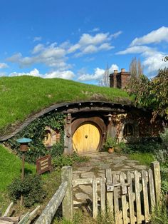 a hobbot house with a wooden fence and green grass on the roof, surrounded by greenery