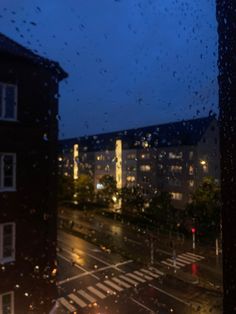 rain is falling down on the street and buildings in the distance, with cars passing by