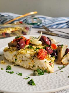 a white plate topped with fish covered in olives