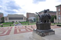 a statue in the middle of a courtyard with people walking around and buildings in the background