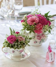 two tea cups with flowers in them sitting on a table