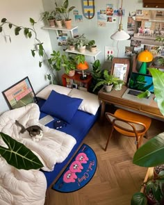 a living room filled with lots of plants next to a desk and computer monitor on top of a wooden floor