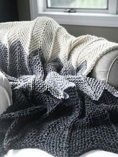 a gray and white knitted blanket sitting on top of a couch next to a window