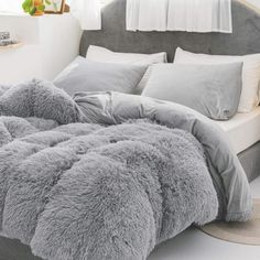 a bed with grey comforter and pillows in a bedroom