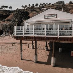 a restaurant on the beach with people sitting at it's tables and in front of the ocean