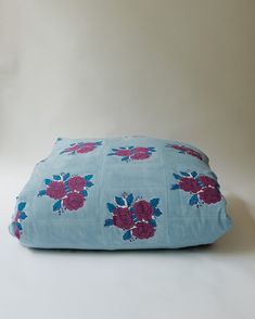 a blue and pink flowered pillow on a white surface with no one around it