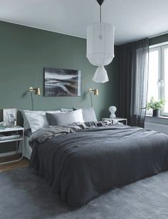 a bedroom with dark green walls and grey carpeted flooring, a large bed in the center