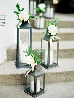 three black lanterns with white flowers and greenery sit on the steps next to each other