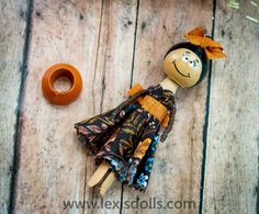 a wooden doll next to an orange donut on a wooden surface with wood planks