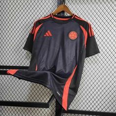 an orange and black soccer jersey hangs on a rack in front of a metal fence