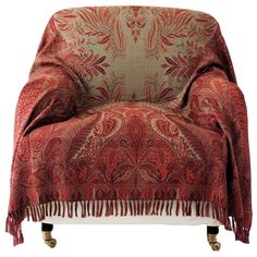 a chair covered in a red and gold paisley print with tassels on the legs