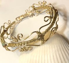 a close up of a gold bracelet on a white seashell with a sea urn in the background