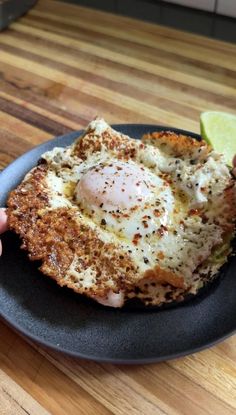 someone is holding up a fried egg on a black plate with lime wedges next to it