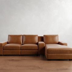 a brown leather couch sitting on top of a hard wood floor next to a white wall