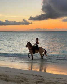 a woman riding a horse on the beach at sunset