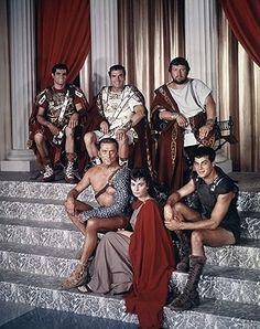 a group of men and women dressed in roman costumes sitting on some steps with red drapes