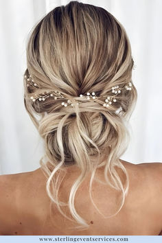 a woman with blonde hair wearing a gold headband and pearls in her hair is seen from the back