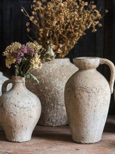 three vases with flowers in them sitting on a table next to other vases