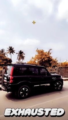 a black suv driving down a street next to palm trees and a yellow kite in the sky