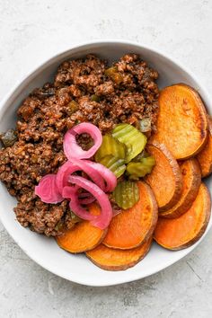 a bowl filled with meat and vegetables on top of a white countertop next to sliced onions