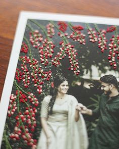 a couple standing next to each other in front of red berries on a tree branch