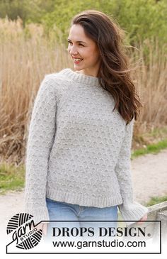 a woman wearing a gray sweater and jeans standing in front of tall grass with her hands on her hips