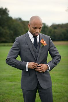 a man in a gray suit and flower boutonniere is standing on the grass