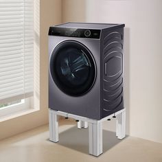 a washing machine sitting on top of a stand in front of a window with blinds