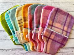 six multicolored plaid oven mitts are lined up on a white wooden surface