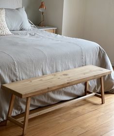 a wooden bench sitting on top of a bed next to a night stand and lamp