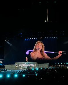 a woman holding a microphone in front of an audience at a concert with lights on