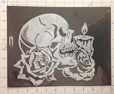 a sticker with a skull and two roses on it, next to a ruler