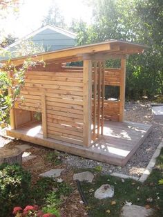 a dog house made out of pallets in the yard with rocks and plants around it