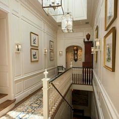 the hallway is decorated in white and has pictures on the wall, chandelier, and stairs