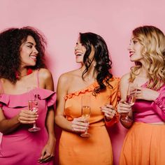 three women in pink and orange dresses holding wine glasses