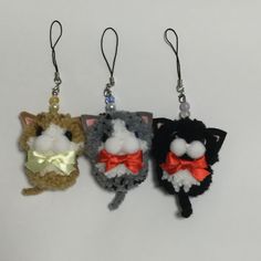 three small stuffed animals hanging from hooks on a white surface, one is wearing a red bow tie and the other has a black cat