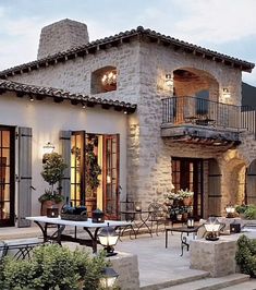 an outdoor patio with tables and chairs next to a stone building at dusk, surrounded by greenery