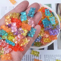 a hand holding a bowl filled with lots of gummy bear beads on top of a book