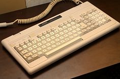 an old computer keyboard sitting on top of a wooden desk next to a telephone cord