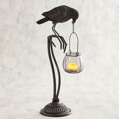 a black bird sitting on top of a metal stand with a candle in it's beak