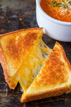 a grilled cheese sandwich cut in half with a bowl of tomato soup behind it