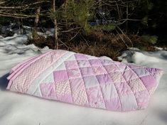 a pink and white quilted sleeping bag laying in the snow next to some trees