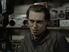 a man wearing glasses and a sweater in a room full of old radio equipment,