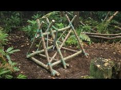 a wooden structure made out of sticks in the middle of some dirt and grass with trees behind it