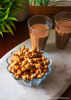 two glasses of chocolate milk and some nuts on a marble platter next to each other