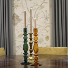 three candles sitting on top of a wooden table in front of a curtained window