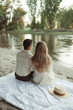 a man and woman sitting on a blanket looking at the water