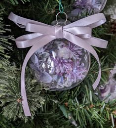 an ornament hanging from a christmas tree decorated with purple flowers and ribbon tied around it