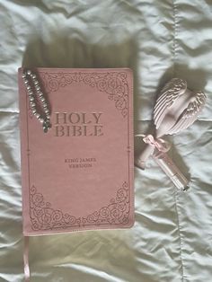 a pink bible laying on top of a bed next to a beaded bracelet and key