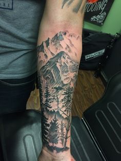 a man's arm with mountains and trees tattoo on the left side of his arm